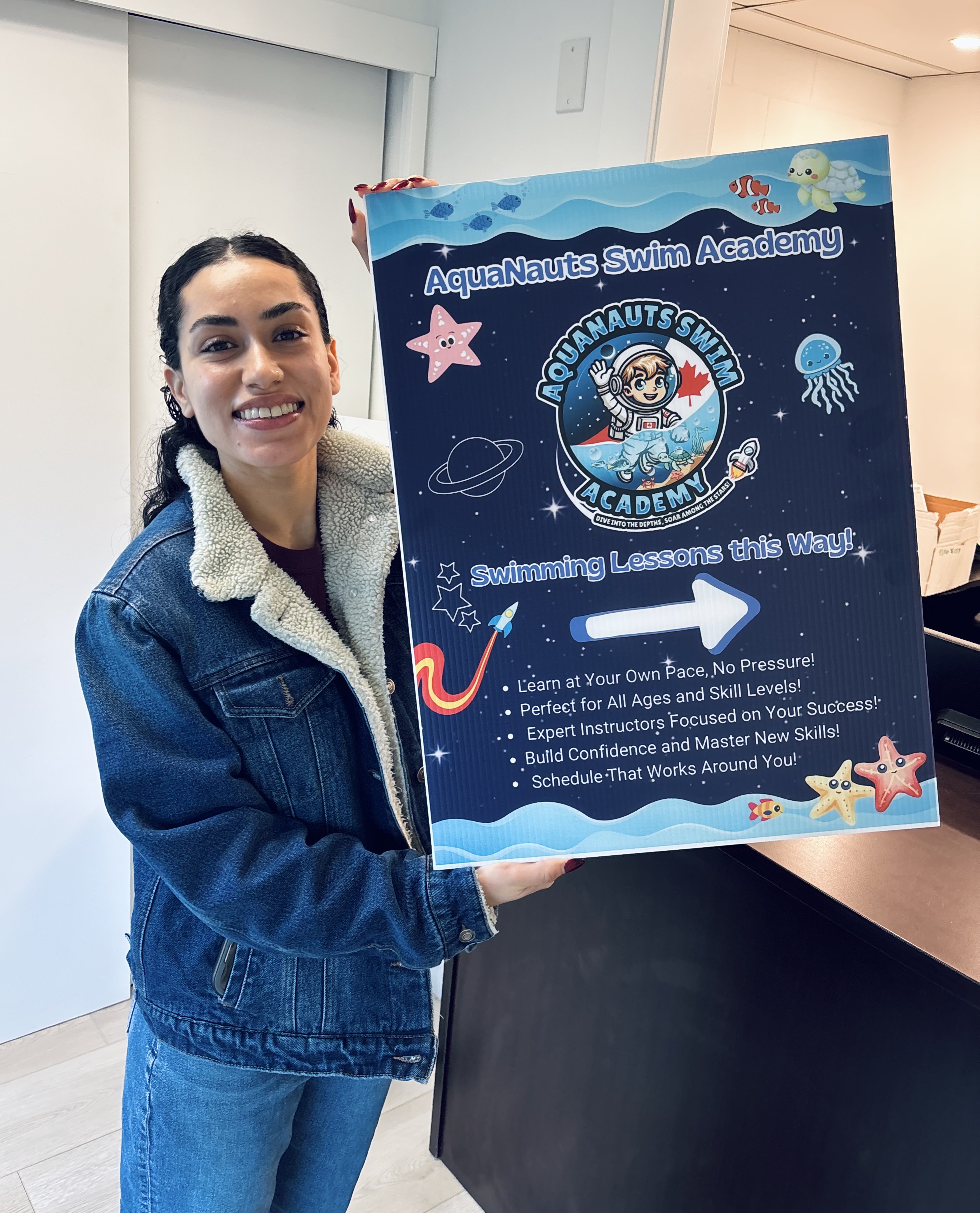 A smiling person holding an Aquanauts Swim Academy sign